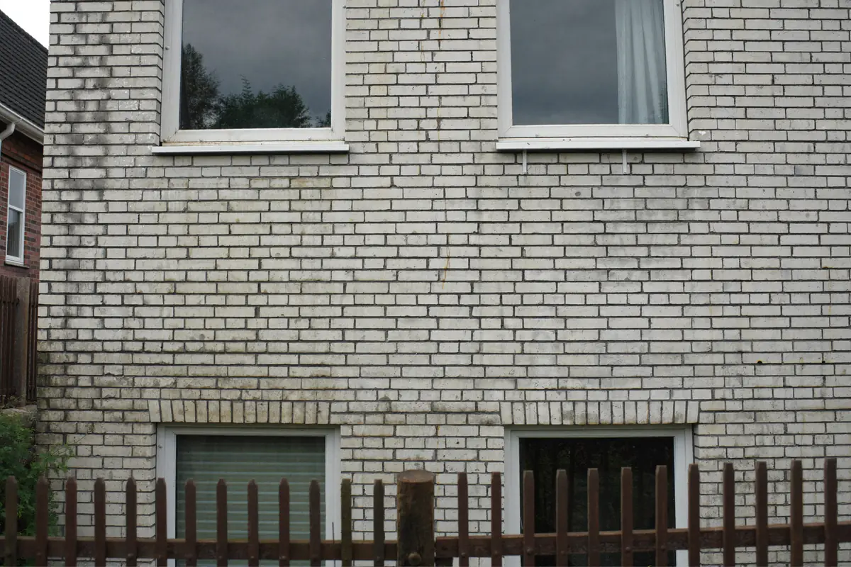 Achtergevel van een jaren-zeventigwoning in lichte kalkzandsteen met vuile strepen onder de kozijnen
