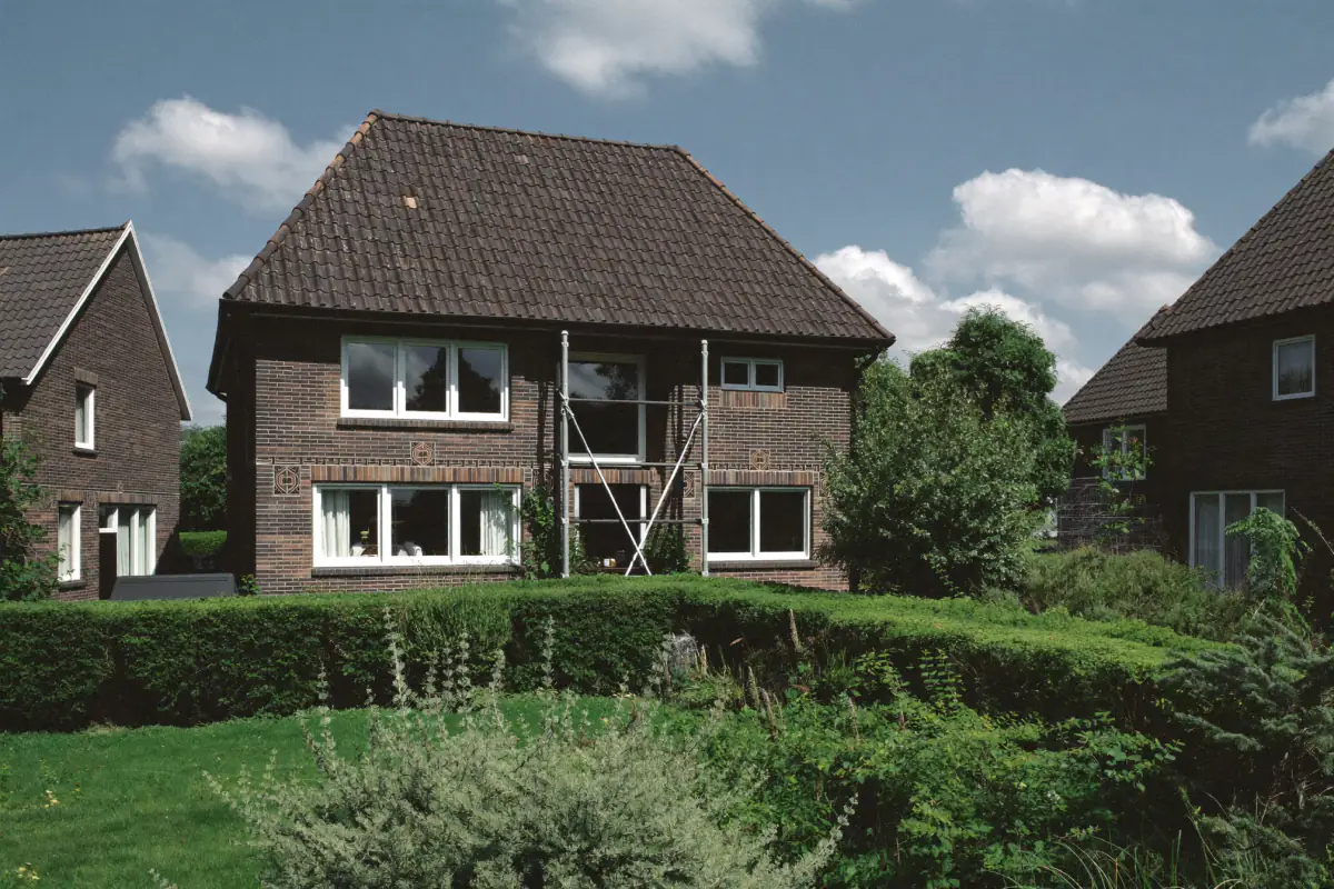 Bakstenen villa uit de jaren twintig met siermetselwerk in een groene villawijk, deels in de steiger