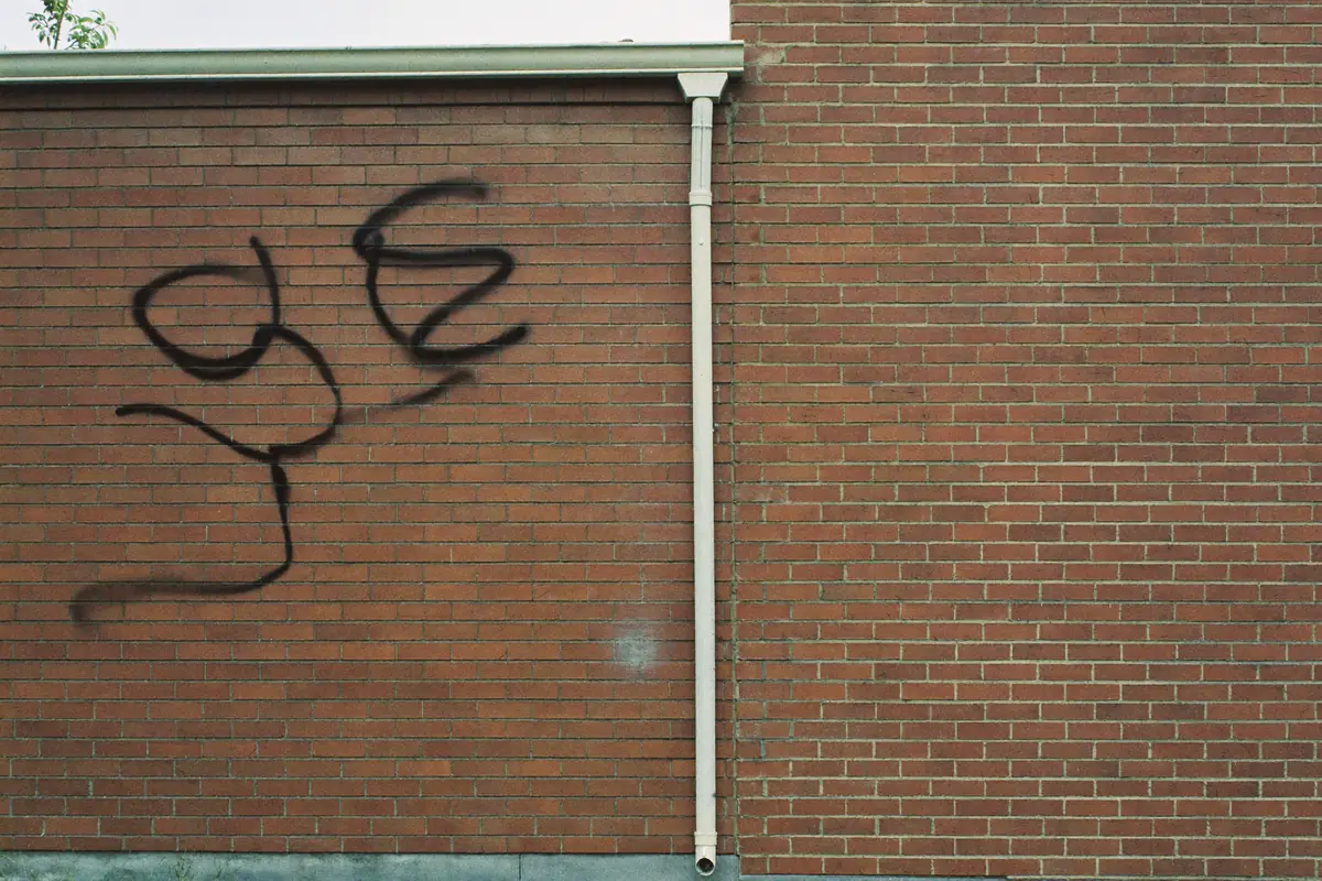 Zwarte spuitverfkrullen op een rode bakstenen zijmuur naast een regenpijp