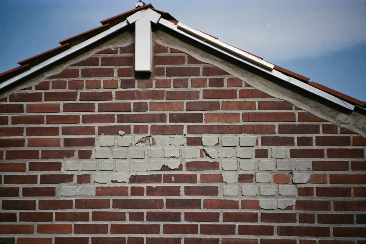 Gevel met afgesprongen en lichter gekleurde stenen na vorstschade onder de topgevel