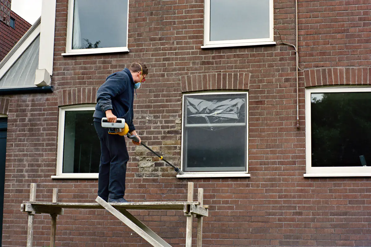 Gevelwerker slijpt met stofafzuiging de oude voegen uit een bakstenen gevel van een jaren-dertigwoning